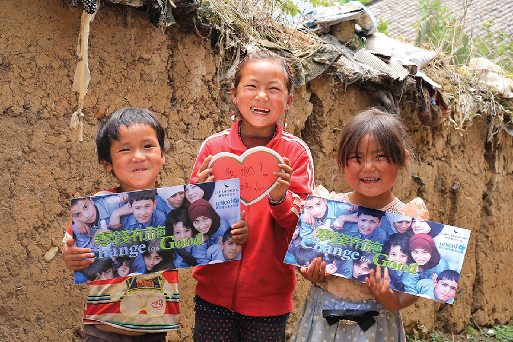 Three happy children smiling and holding a Cathay Pacific and Unicef Hong Kong Change for Good poster.