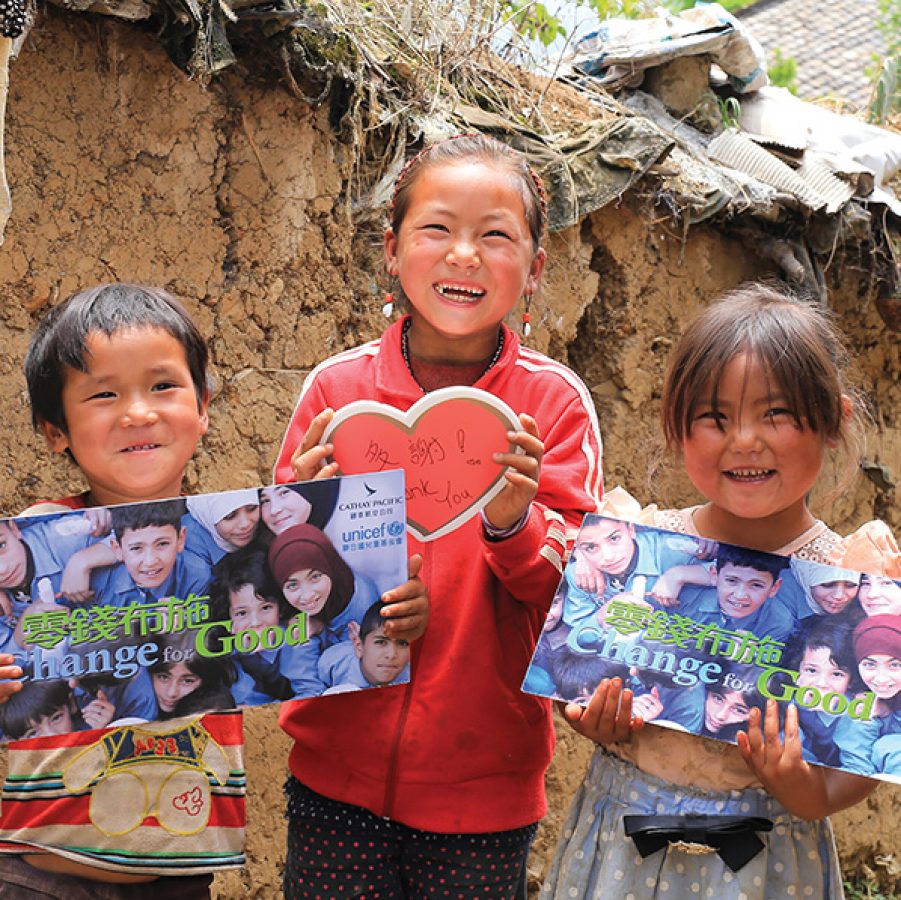 Three happy children smiling and holding a Cathay Pacific and Unicef Hong Kong Change for Good poster.