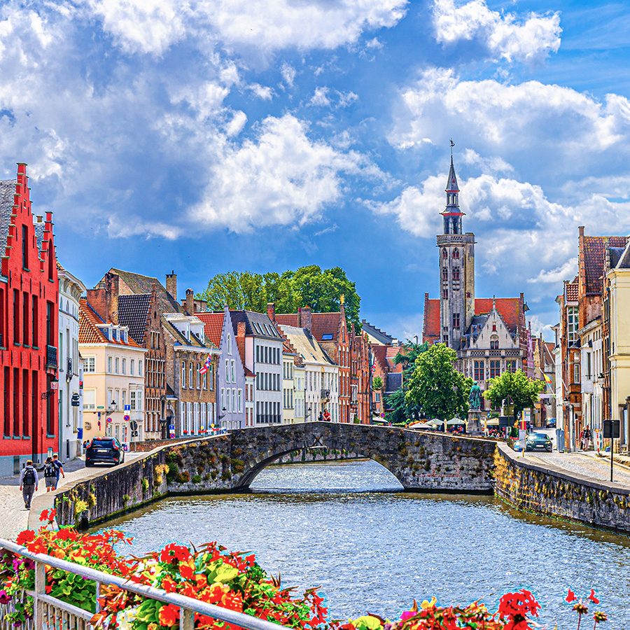 Colourful and pastel buildings sit along the canal in Bruges on a sunny day.