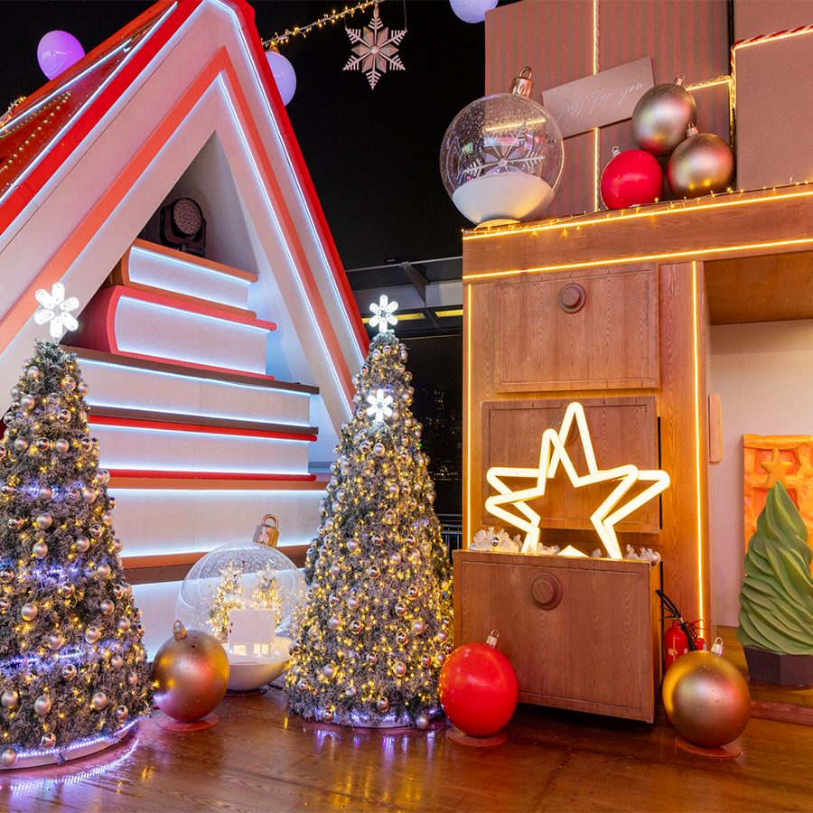  A pile of oversized books are arranged to look like a log cabin, with two Christmas trees standing in front of them, at the Big Little Christmas installation at Harbour City.