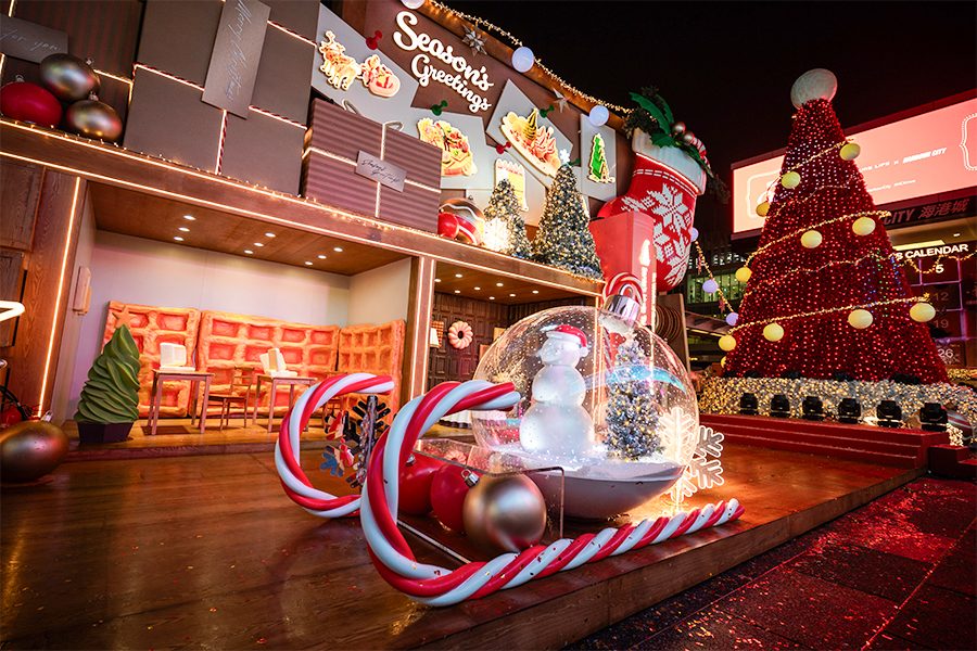 On an outdoor platform, a giant Christmas bauble and two candy canes are arranged to look like a sleigh. Behind them, a sign reads “season’s greetings”. 