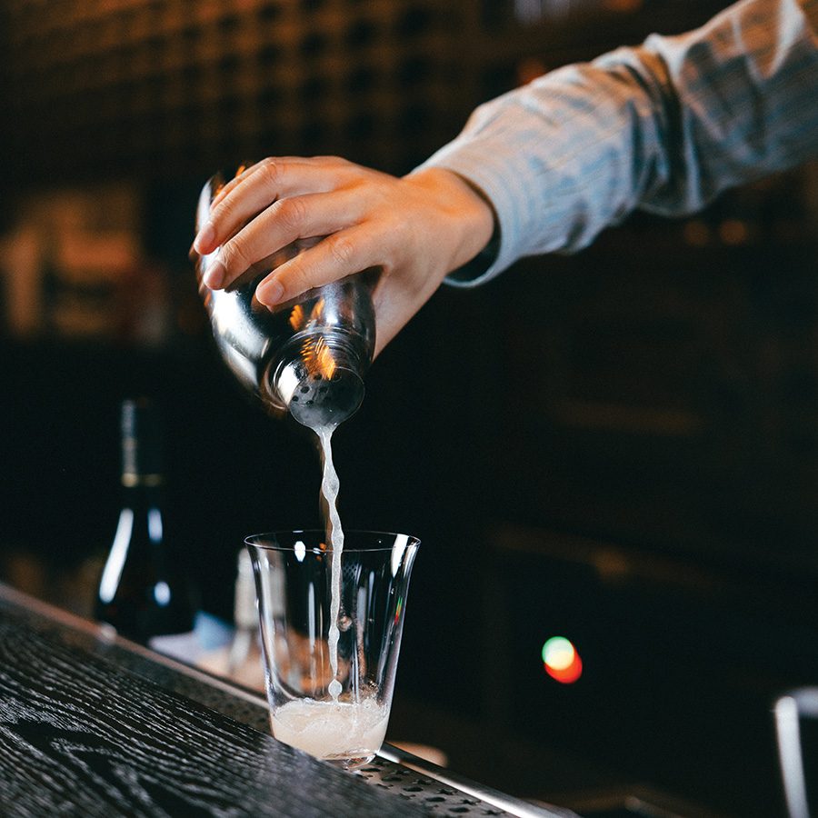 A white drink being poured out of a cocktail shaker.