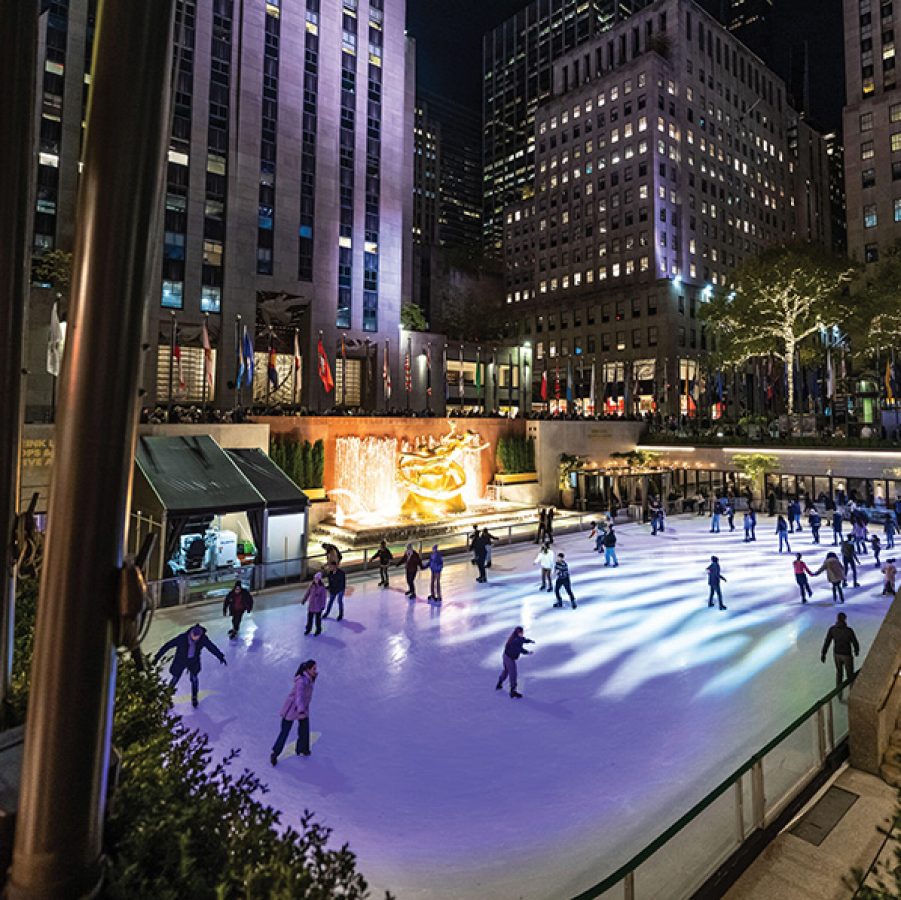 People ice skating at an outdoor rink at the Rockerfeller Center in New York City at night.
