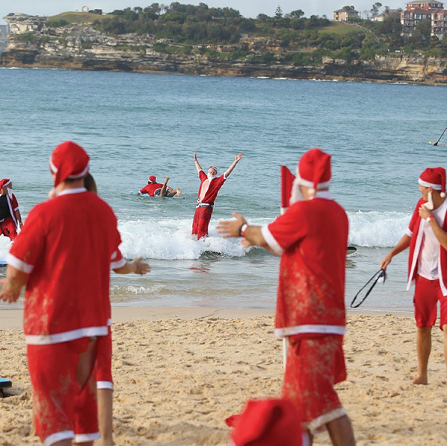 A crowd of men dressed in Santa Claus outfits swimming at Bondi Beach in Sydney during daytime.