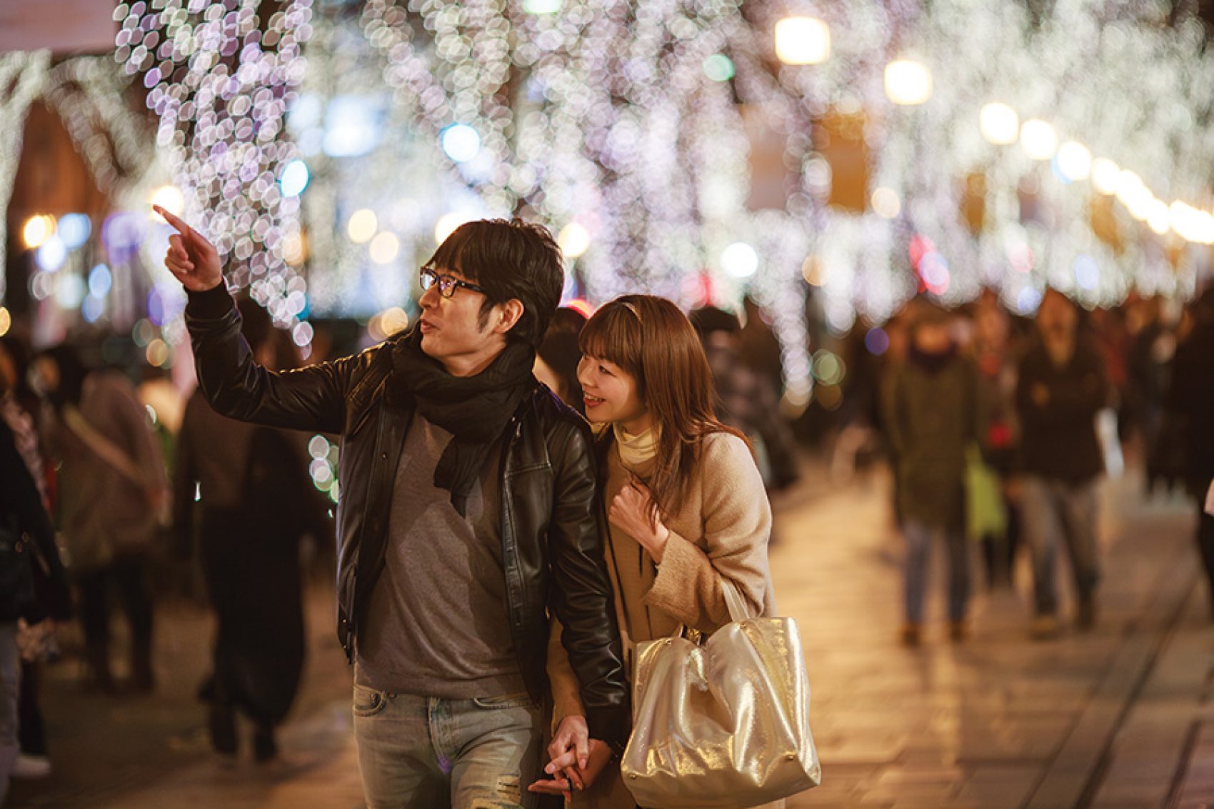 A couple walking holding hands and admiring Christmas lights and decorations in Tokyo at night.