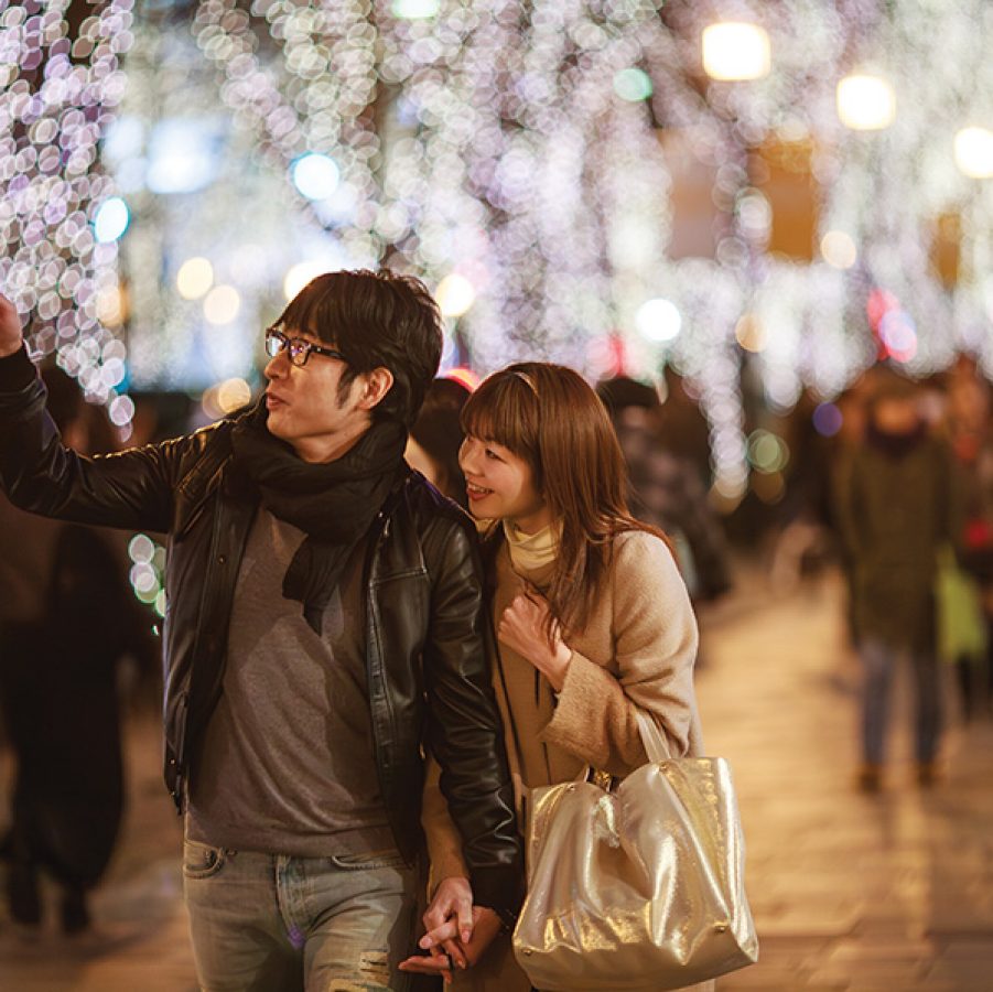 A couple walking holding hands and admiring Christmas lights and decorations in Tokyo at night.