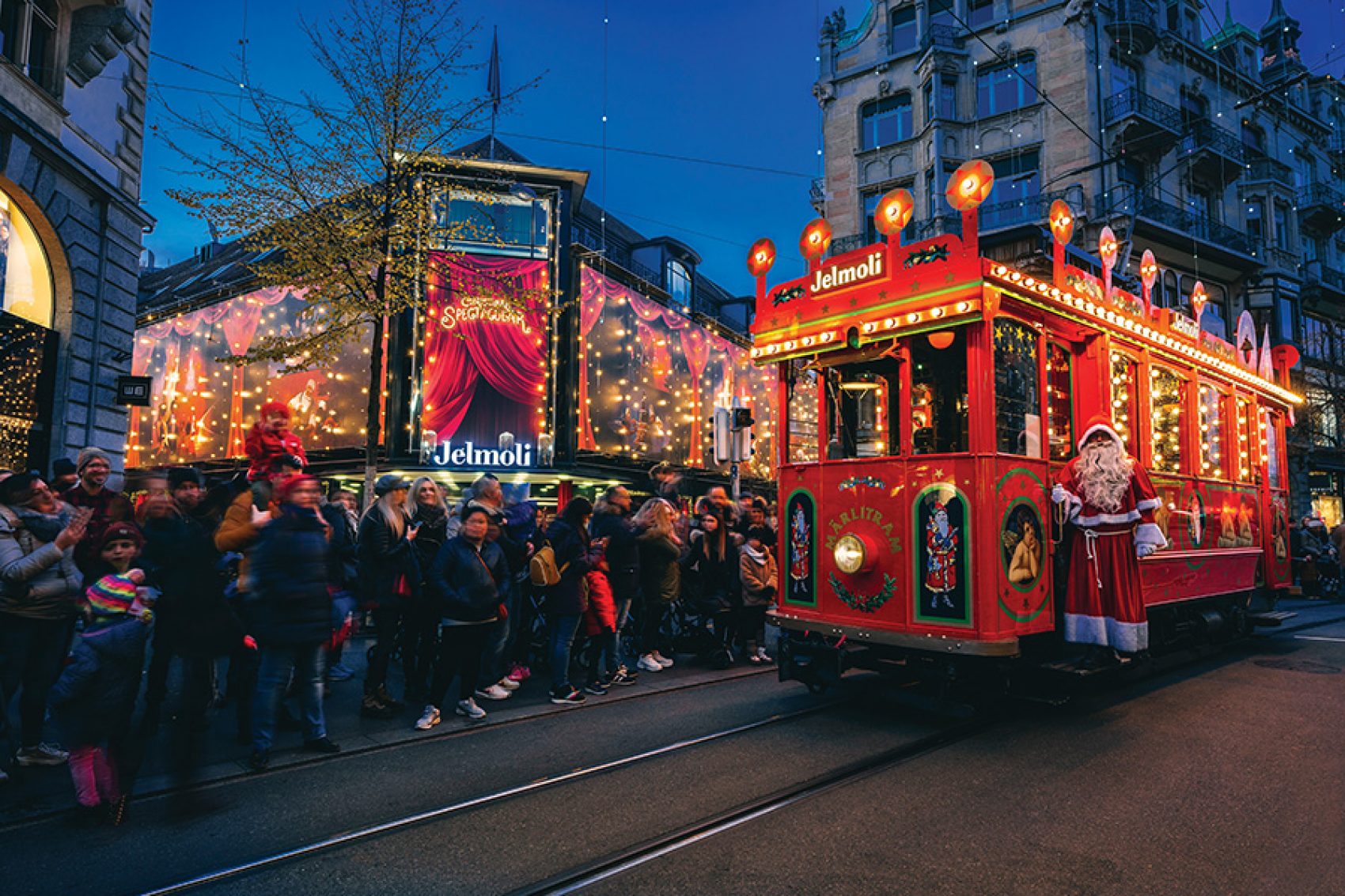 A crowd gathering by the tram tracks to watch the red illuminated Märlitram pass by with Santa Claus in Zurich.