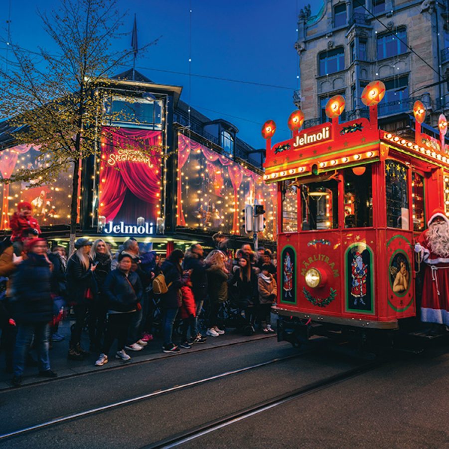 A crowd gathering by the tram tracks to watch the red illuminated Märlitram pass by with Santa Claus in Zurich.