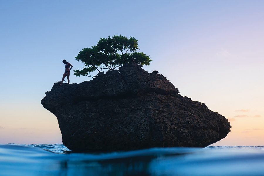 Silhouetted woman stands on the edge of a rock looking down into the ocean.
