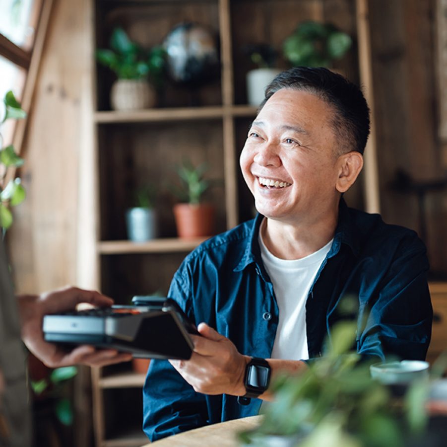 A man happily laughing with a server while making a contactless payment with his smartphone