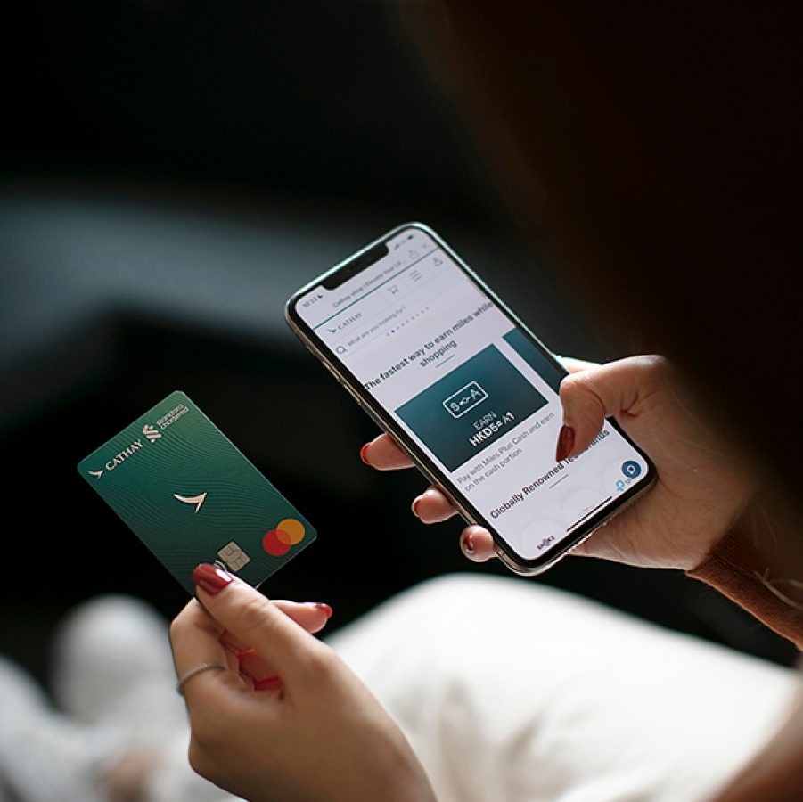 A close-up of a woman holding a Standard Chartered Cathay Mastercard co-branded credit card while holding a smart phone