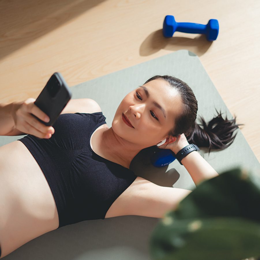 Alt text: A woman exercising on a yoga mat with a dumbbell on the side, smiling while looking at her smartphone