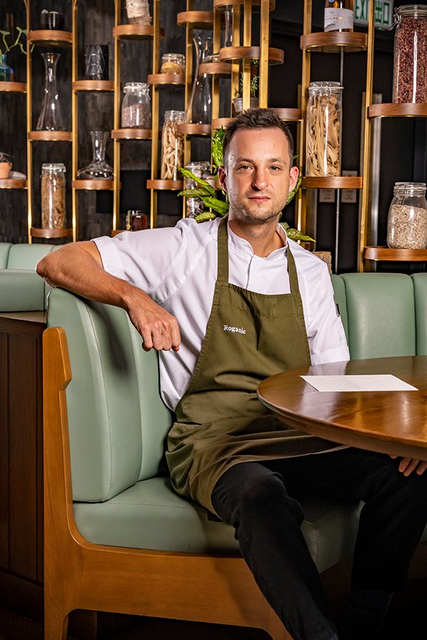 Adam Catterall, head chef at Roganic, sits at a restaurant booth and poses for a picture.