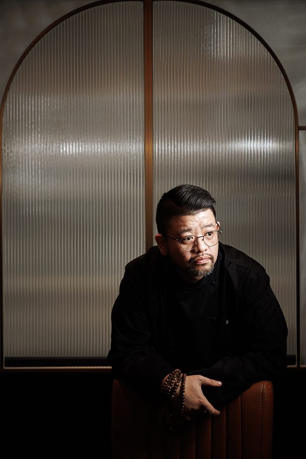 Silas Li, executive chef at Hong Kong Cuisine 1983, sits against a dimly lit wall and poses for a picture.