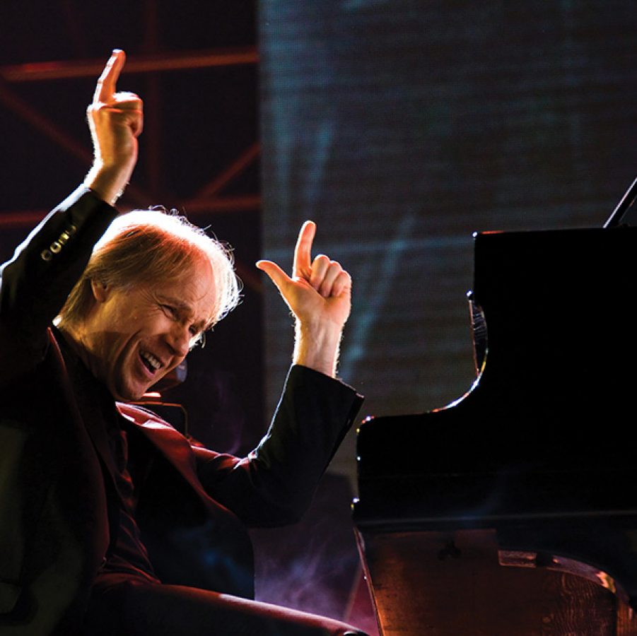 French pianist Richard Clayderman on the piano, laughing on stage.