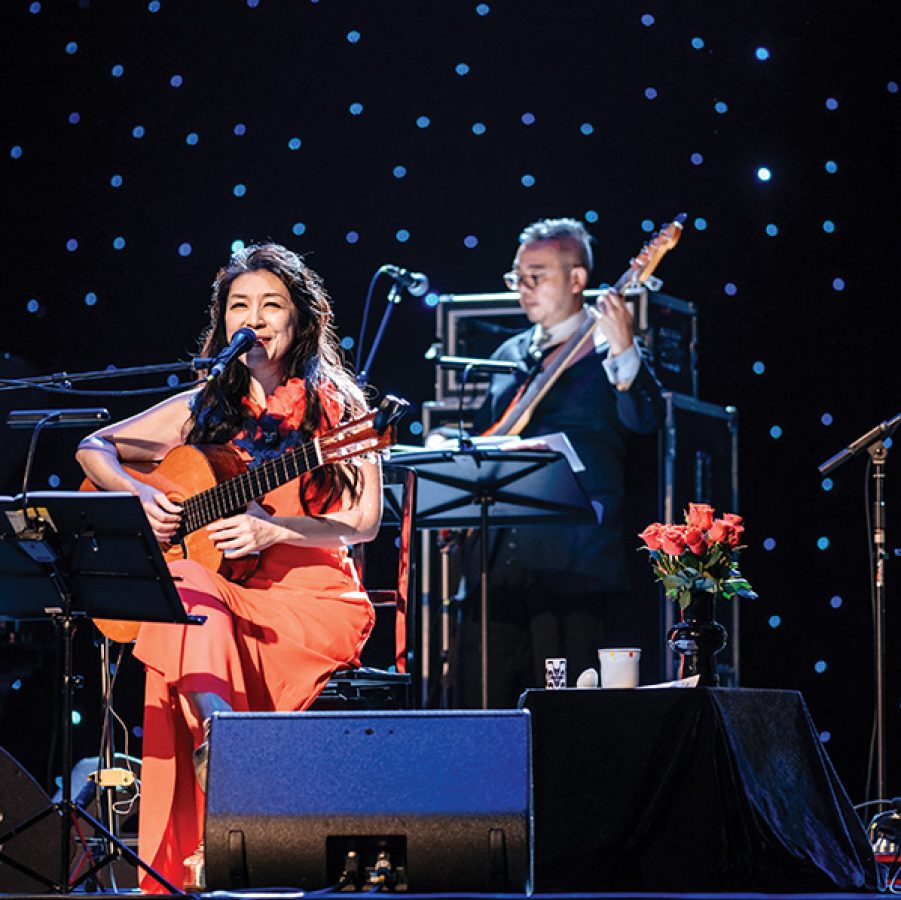 Japanese Brazilian singer Lisa Ono performs with a guitar on stage.