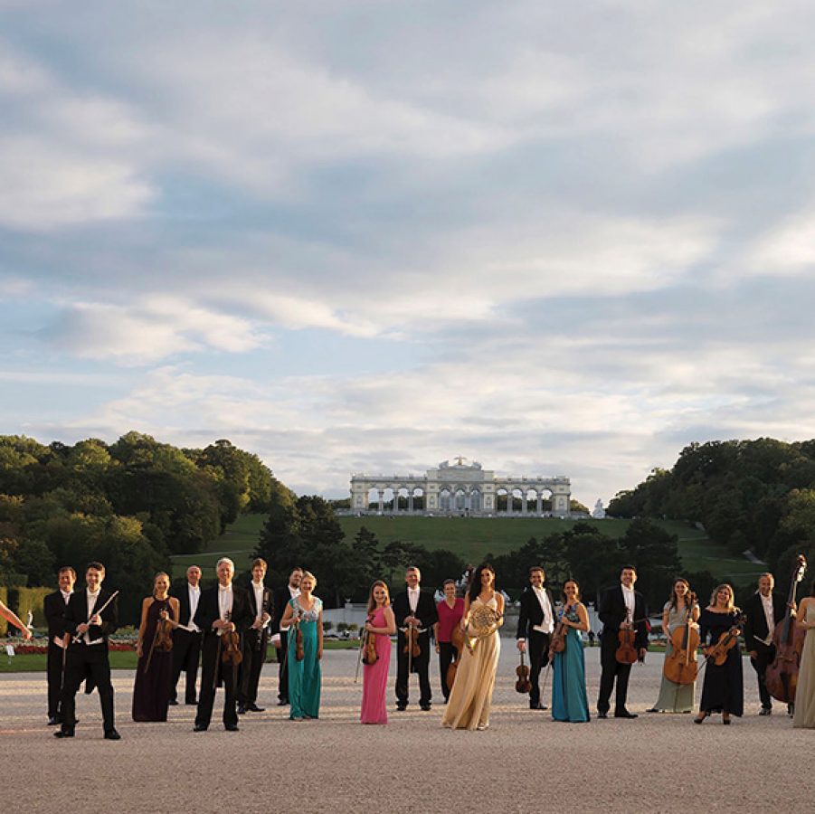 A photo of performers from the Schönbrunn Palace Orchestra Vienna dressed in a colourful ensemble in the open courtyard at Schönbrunn Palace, Vienna.