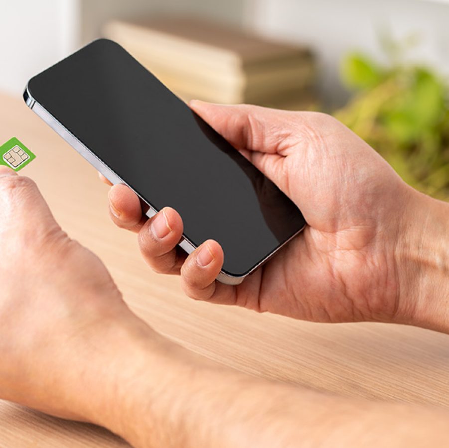 A person holding a phone and a SIM card side by side. 
