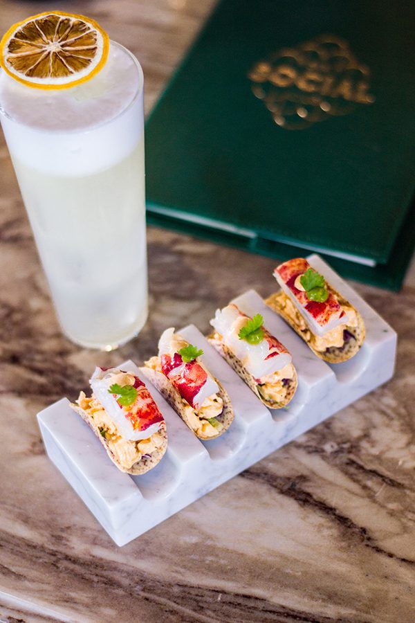 A top-down view of a tall glass of cocktail and bar snacks, served at BKK Social in Bangkok.