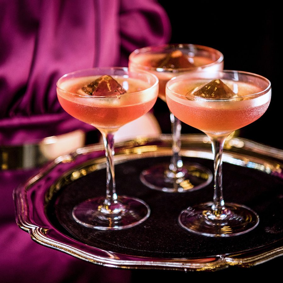 A close-up of a woman holding three glasses of cocktails, served at BKK Social in Bangkok.