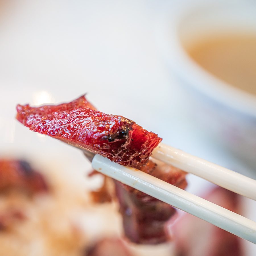 A pair of chopsticks holding a piece of char siu. 