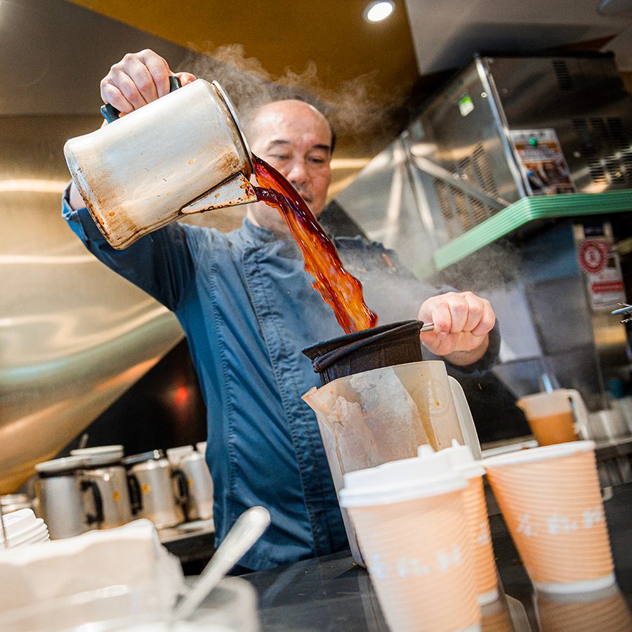 A man pouring hot milk tea into a stocking-like cotton bag.