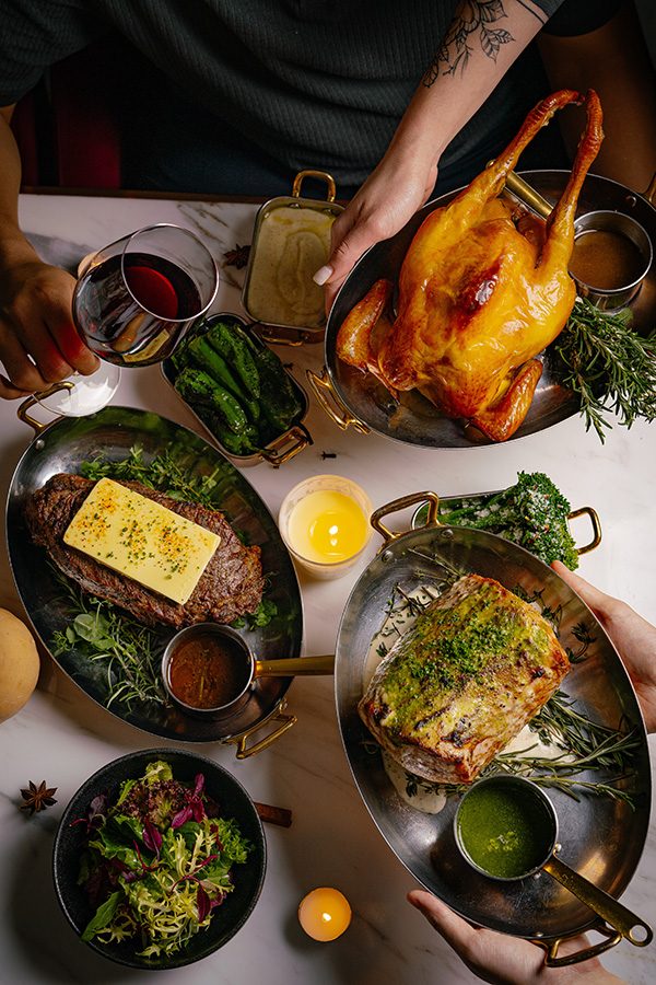 A top down view of a dining table with a spread of various festive dishes served at Bianco & Rosso in Central, featuring a whole three-yellow chicken, steak and fish.