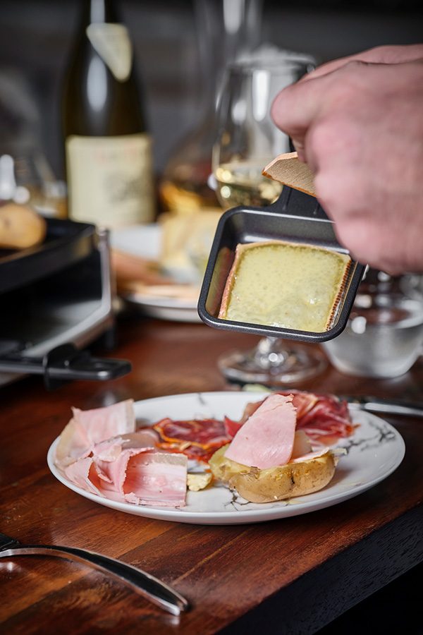  A close up of a person holding a mini cheese raclette over a plate of cold cuts and bread with wine on the dining tabe, served at ThinkWine in Soho, Central.