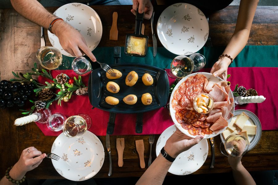 A top down view of a group of people sharing food, coldcuts, cheese and wine at a dining table with Christmas decorations at ThinkWine