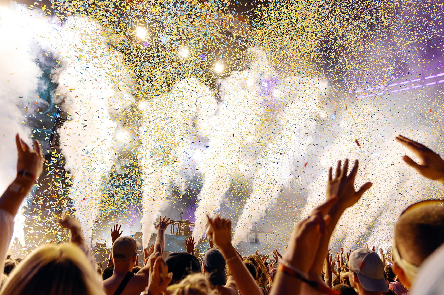 People raising arms at a concert as confetti streams down. 
