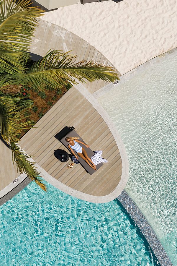A hotel guest relaxing at Crystalbrook Riley’s lagoon-style outdoor pool, which also features a manmade beach. 