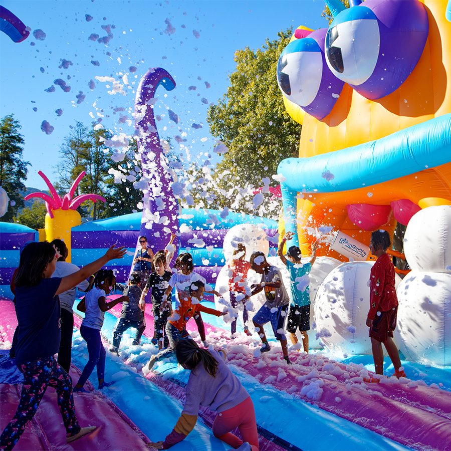 People bouncing on an orange and blue bouncy castle with confetti.