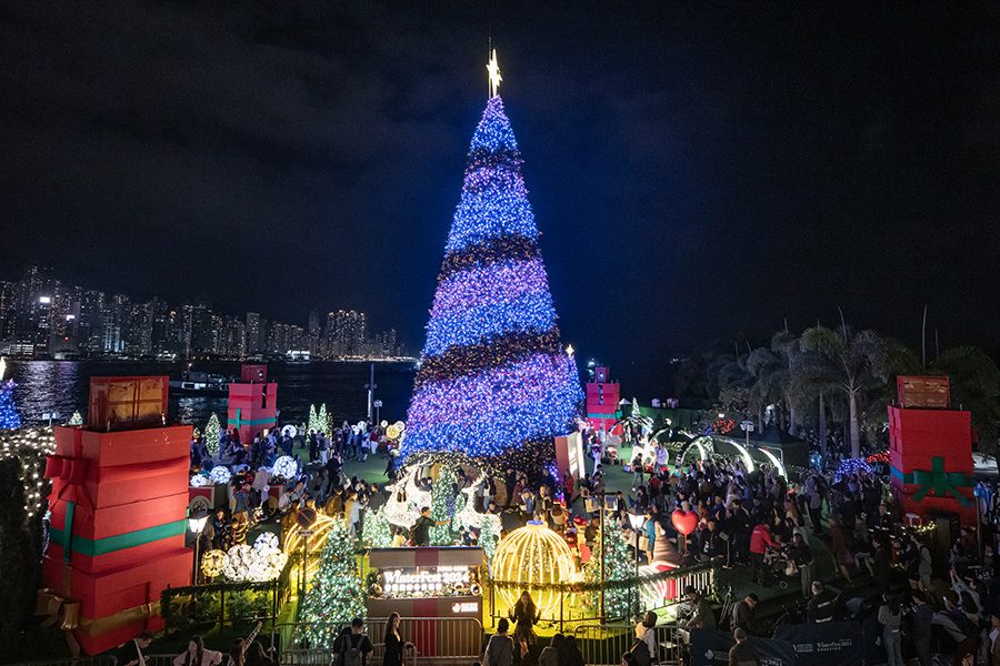 An illuminated Christmas tree with a view of the Hong Kong skyline.
