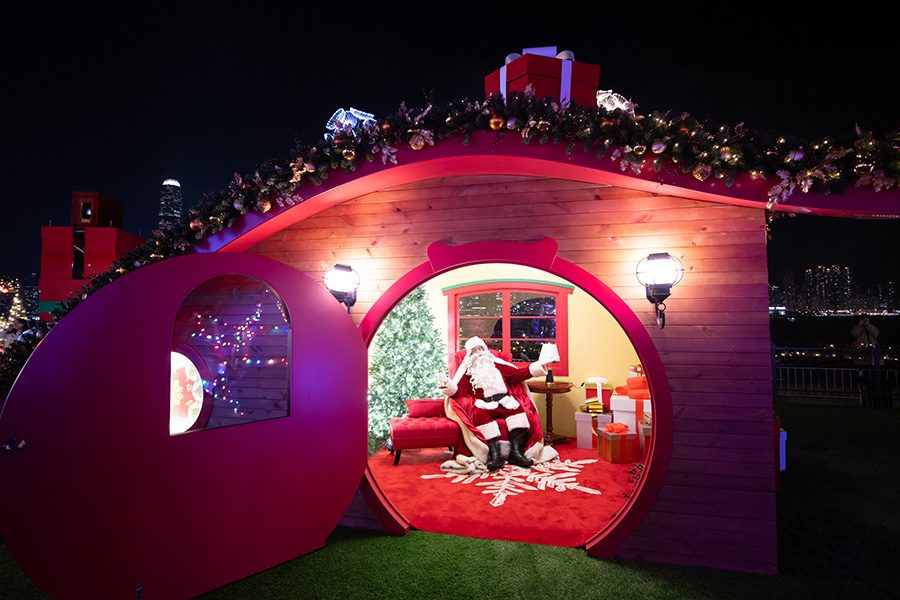 Santa Claus waving hello from inside a faux log cabin.