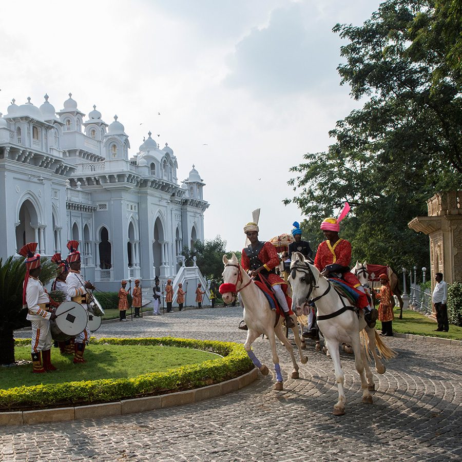 The courtyard outside Taj Falaknuma Palace at daytime. Royal soldiers ride horses and an army band performs.