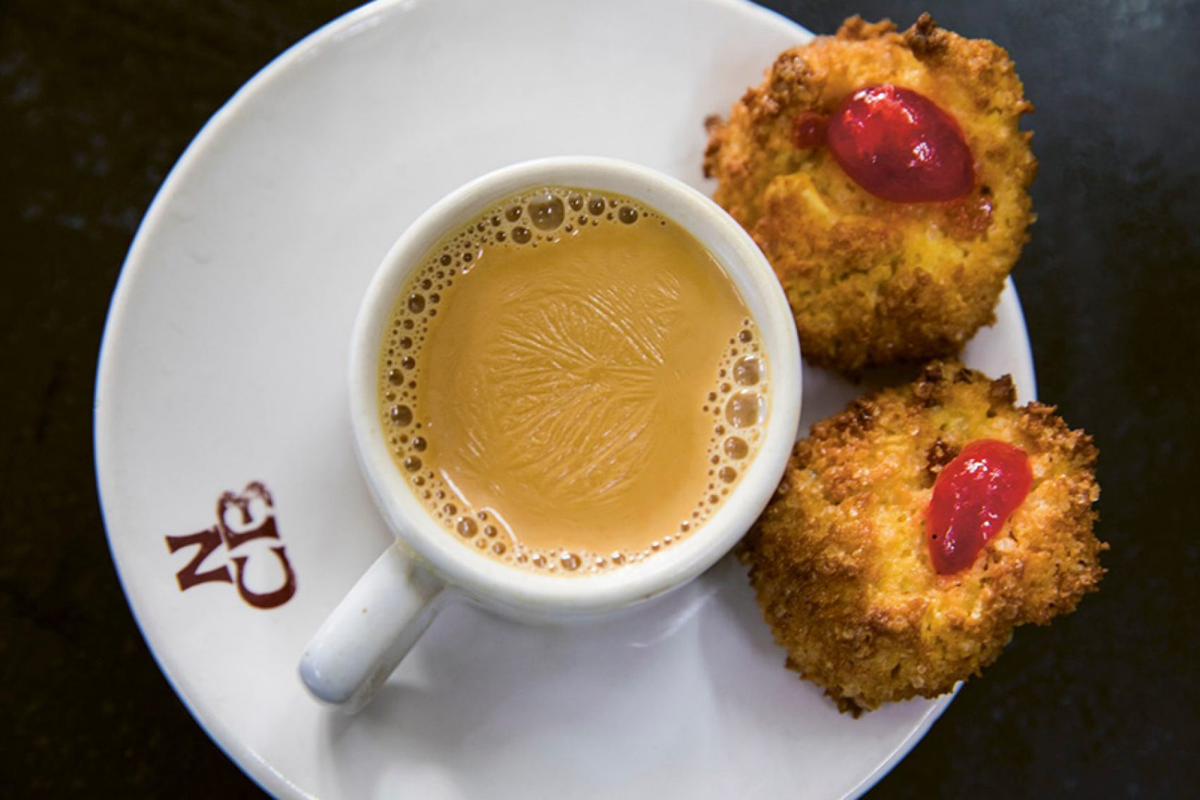 A topdown view of a cup of Irani chai served with two pieces of Osmania biscuits at Nimrah Cafe & Bakery in Hyderabad, India.