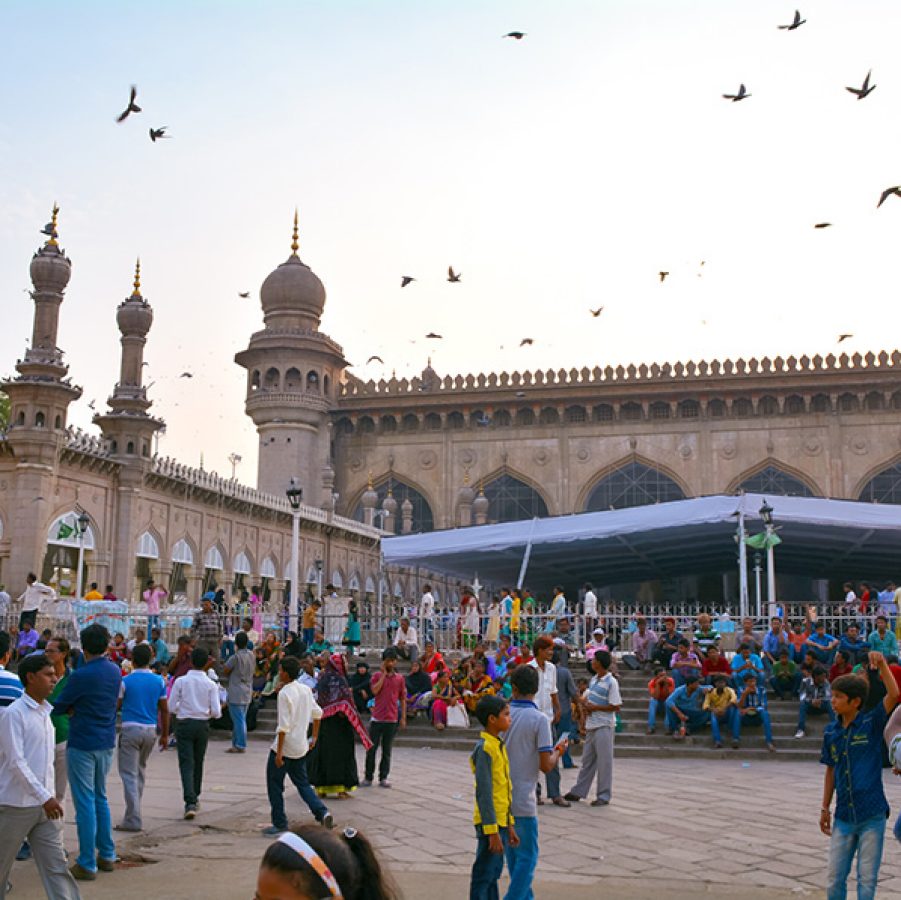  A crowd standing outside of the Mecca Masjid mosque at daytime as birds fly above, in Hyderabad, India.