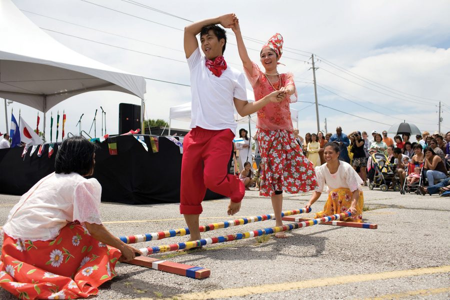 A man and a woman dance the tinikling between two colourful poles held by two crouching women in the daytime in Cebu.