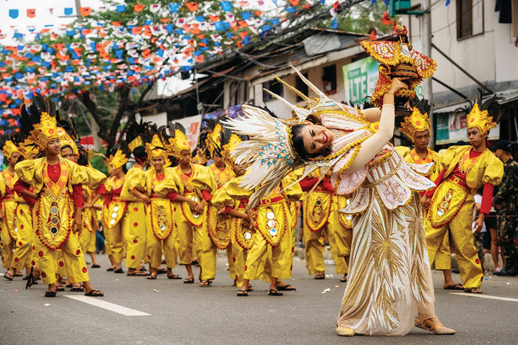 A woman in a white headdress leads a procession of men in yellow costumes during the Sinulog Festival.