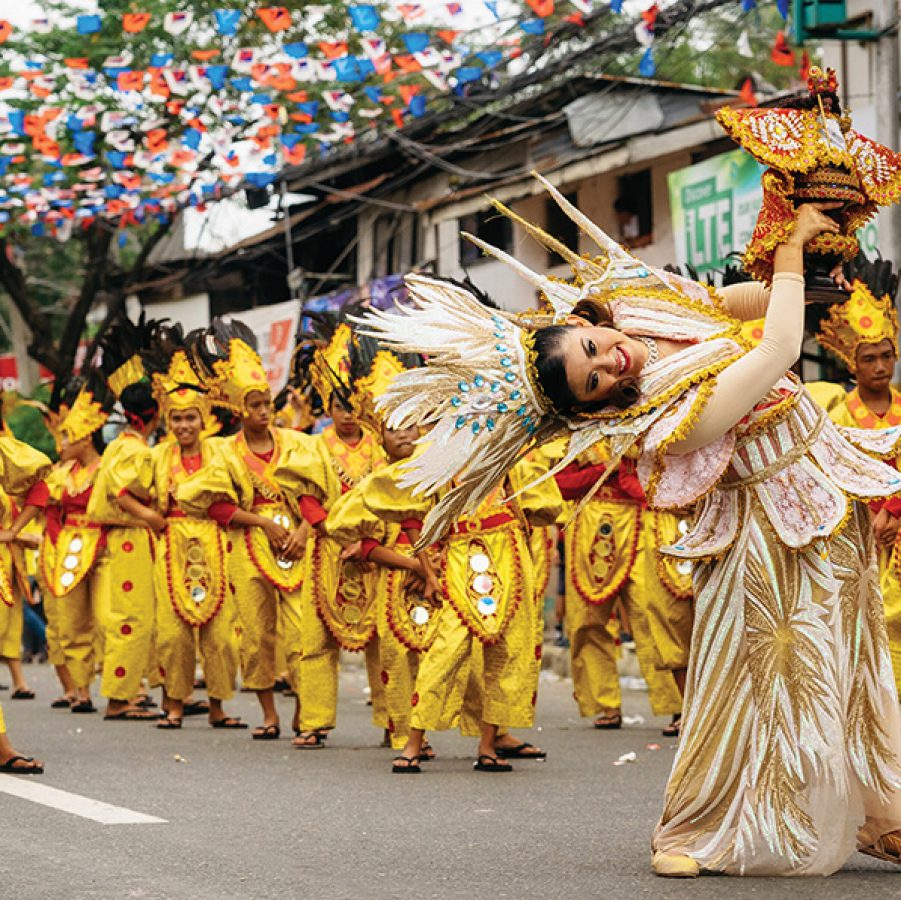 A woman in a white headdress leads a procession of men in yellow costumes during the Sinulog Festival.