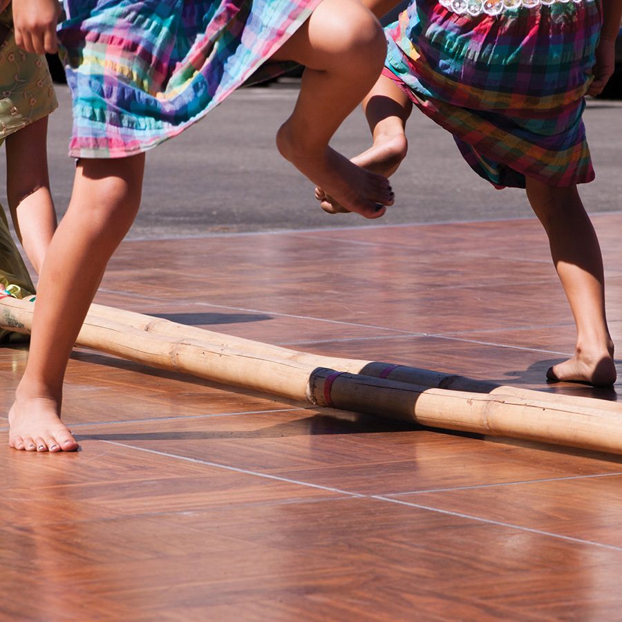 Closeup of tinikling dancers’ legs crossing bamboo poles in the daytime. 