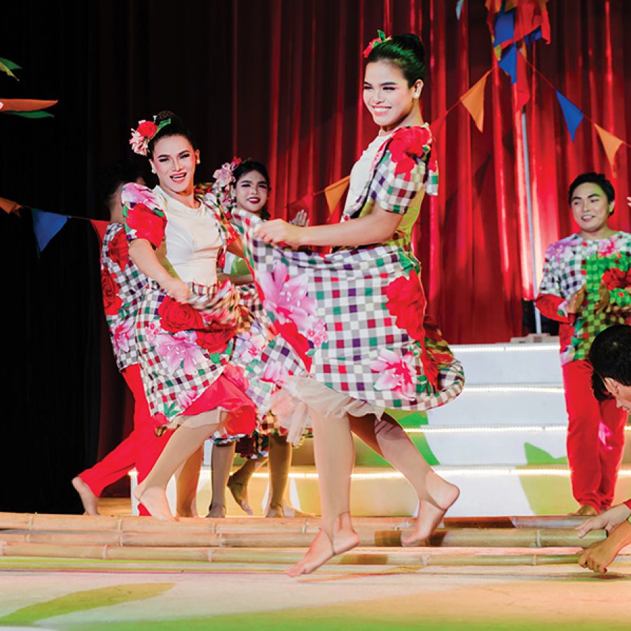 Tinikling dancers in red patterned dresses onstage at the White Note Pavilion.