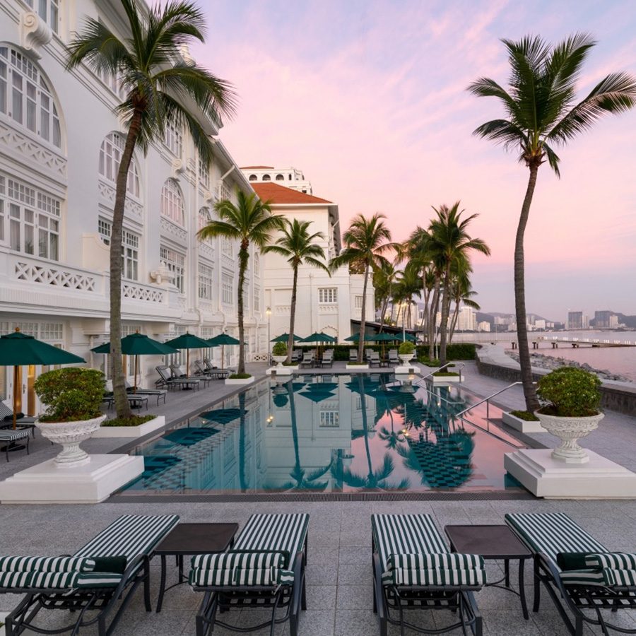 A view of palm trees and the outdoor pool during sunset at Eastern and Oriental hotel in Penang. 