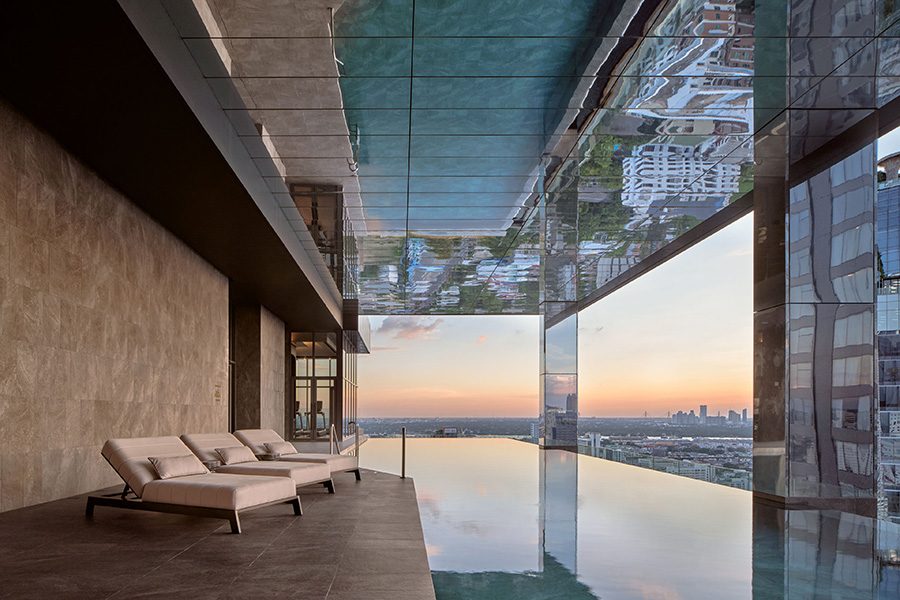 The open air indoor infinity pool at InterContinental Bangkok Sukhumvit with plush lounge chairs and panoramic views of Bangkok city.