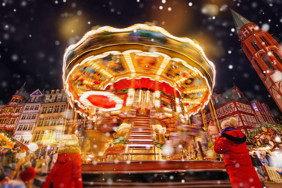 A crowd watching a moving carousel with Christmas decoration and snow falling at a Christmas market in Frankfurt. 