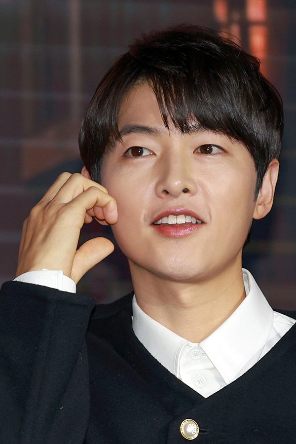 Male Korean star makes a cheek heart gesture with one hand.