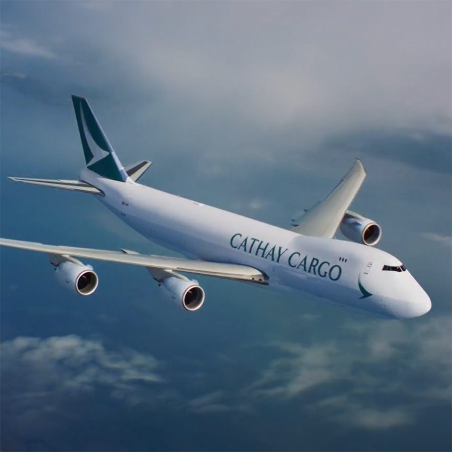 A Cathay Cargo aircraft flying over clouds in the daytime. 