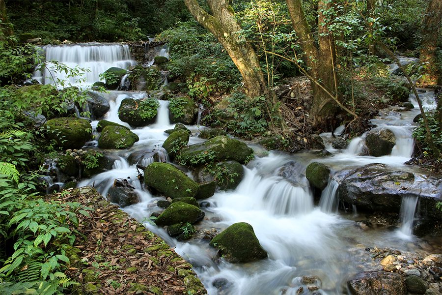 A waterfall over mossy boulders at Shivapuri Nagarjun National Park, Nepal, in the daytime.