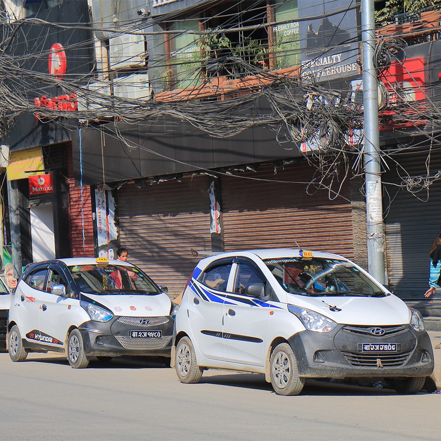 Two taxis parked on a street in Kathmandu in the daytime.