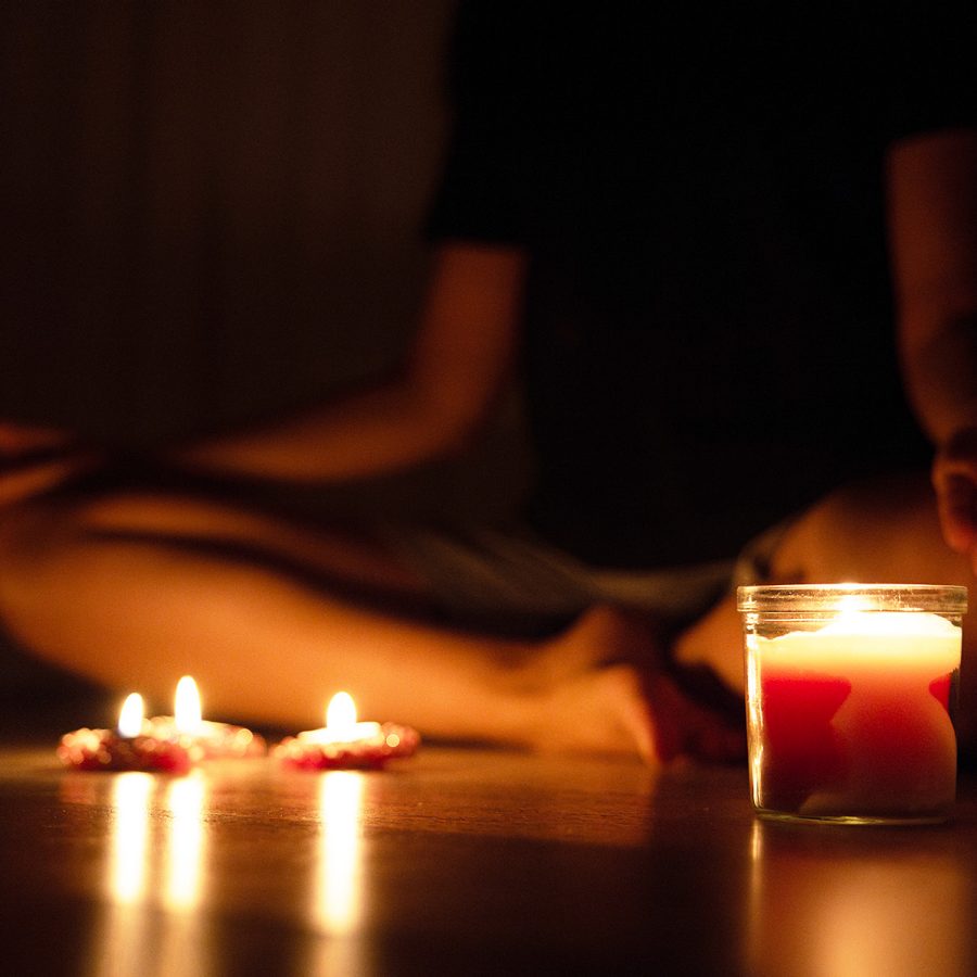 A person meditates in the dark by candlelight, something one can experience during a dark room retreat at Bali’s Samyama Retreat